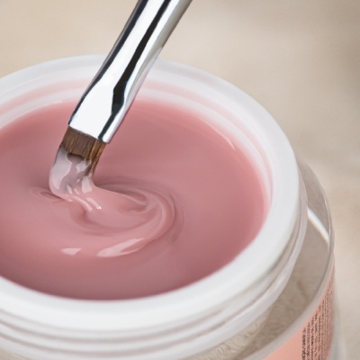 Pote aberto com creme rosado e pincel a misturar o produto.