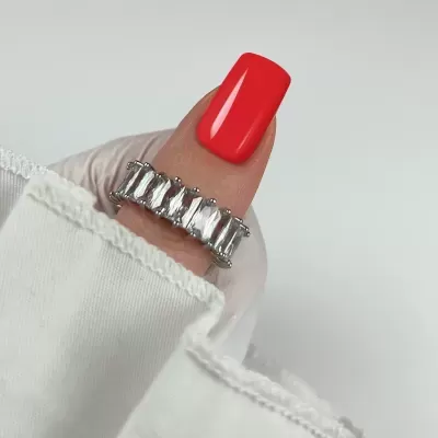 Anel prateado com pedras transparentes num dedo com unha vermelha e manga branca