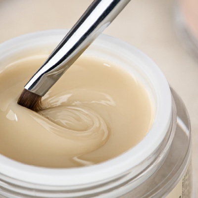 Frasco aberto de creme bege claro com pincel metálico mergulhado no creme
