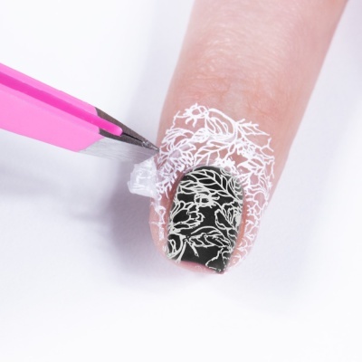 Unha decorada preta e branca com pinça rosa retirando adesivo transparente