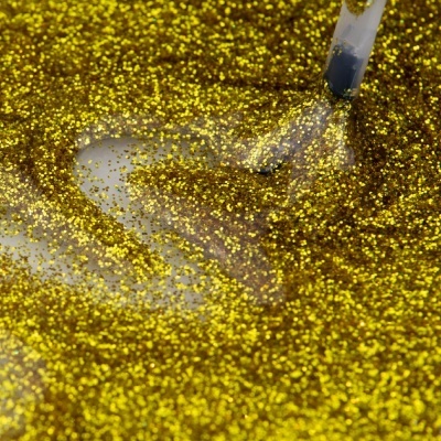 Superfície coberta com glitter dourado brilhante e pincel transparente fazendo marcas