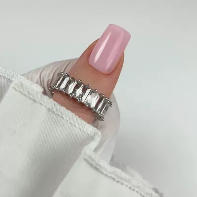 Anel prateado com pedras transparentes em dedo com unha rosa polida e manga branca