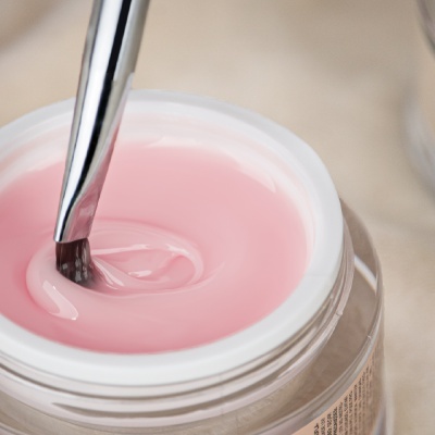 Pote com creme rosa e pincel metálico imerso no creme