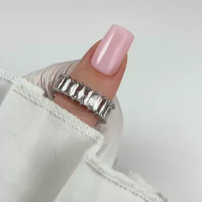 Anel prateado com pedras transparentes e unha rosa claro numa mão com manga branca