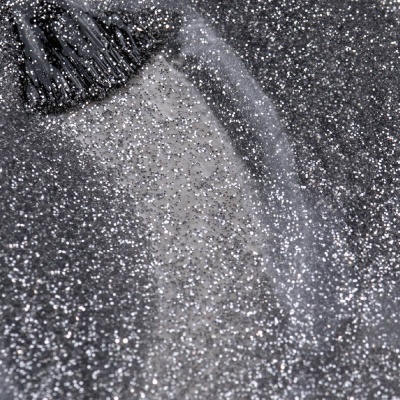 Pincel a aplicar verniz com glitter prateado em superfície com glitter.