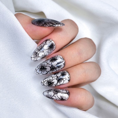 Unhas artificiais com padrão floral preto e fundo prateado sobre tecido branco