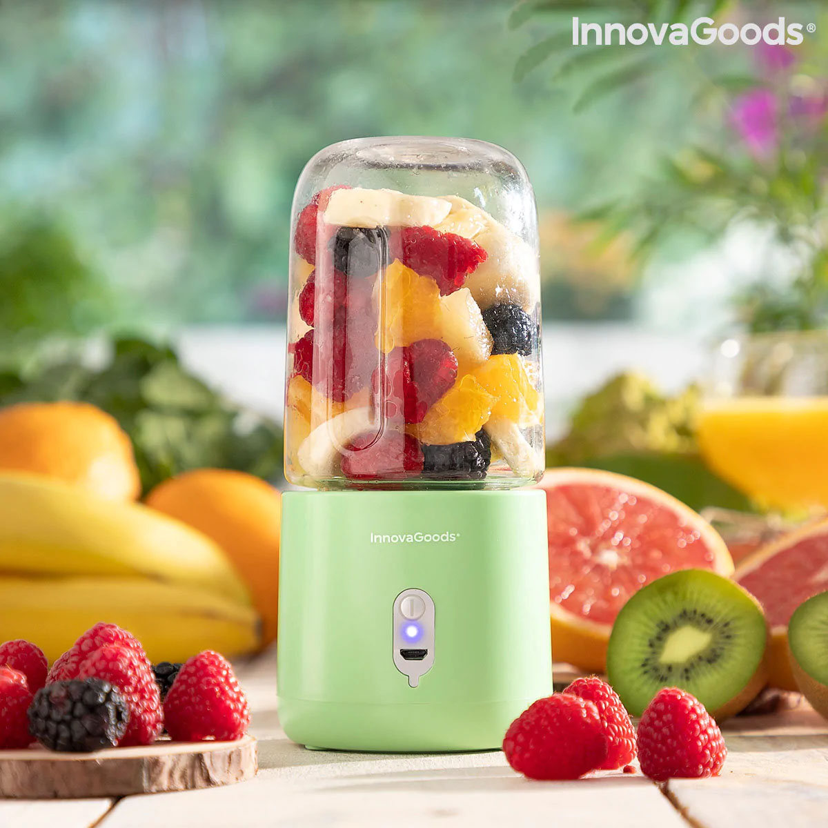 Liquidificador portátil verde com frutas dentro e frutas ao redor em superfície de madeira