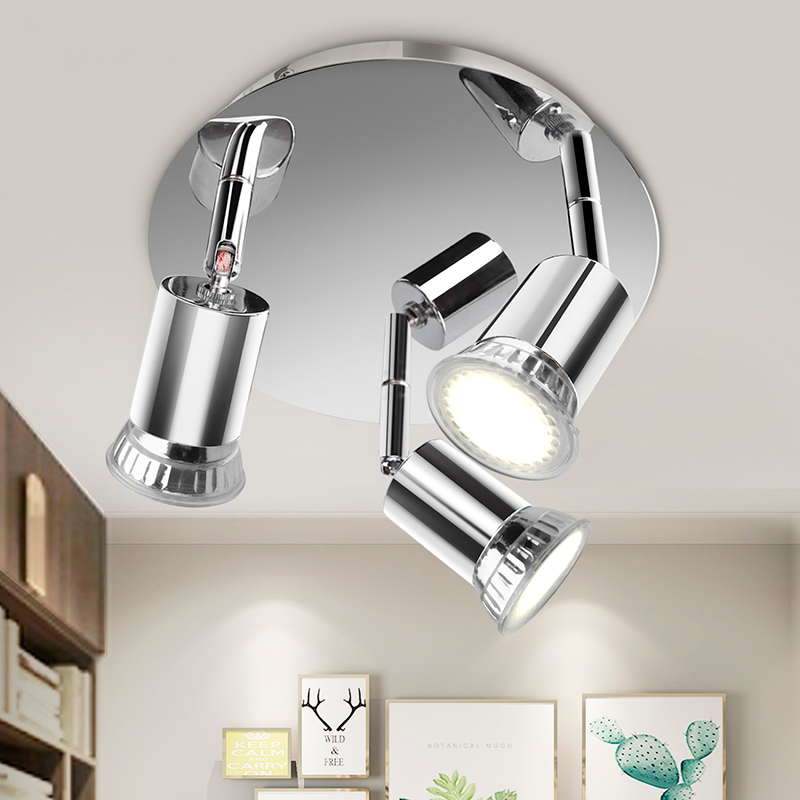 Candeeiro de teto com três focos de luz metálicos cromados em ambiente com quadros de plantas na parede