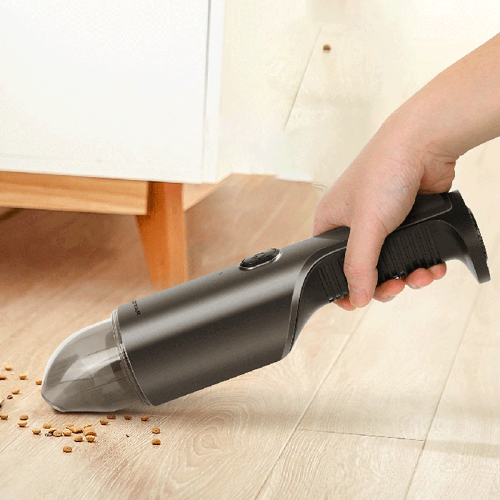 Aspirador portátil preto com depósito transparente a aspirar migalhas em chão de madeira clara
