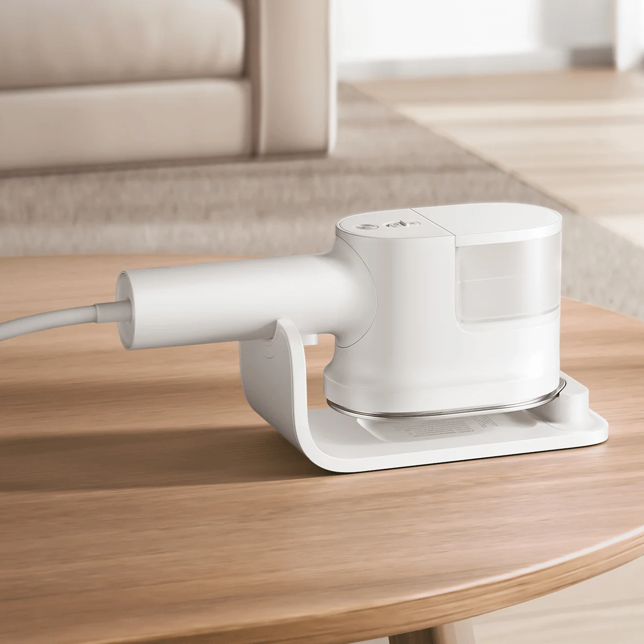 Ferro de engomar a vapor branco numa base sobre mesa de madeira clara, ao fundo sofá bege e chão de madeira clara com tapete cinza.