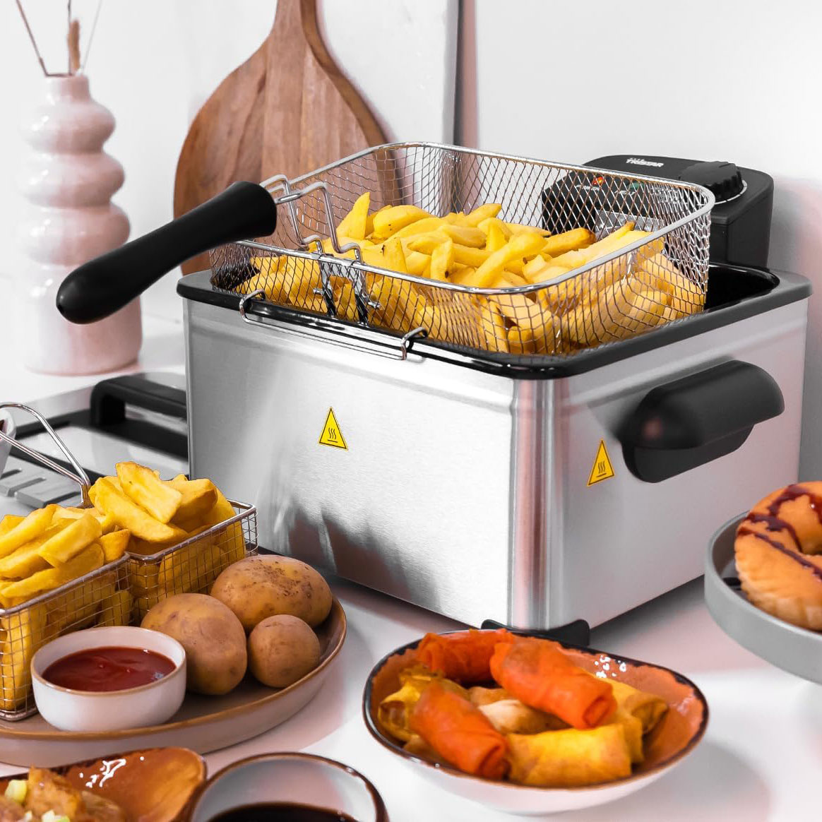 Fritadeira elétrica com batatas fritas e vários pratos de comida numa cozinha.