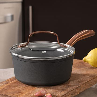 Panela preta com tampa de vidro e pega de metal cobre sobre tábua de madeira com alho e limão