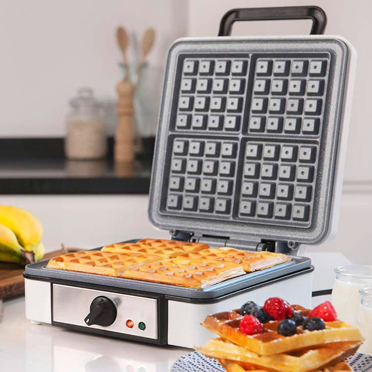 Máquina de waffles com waffles dourados e frutas na cozinha