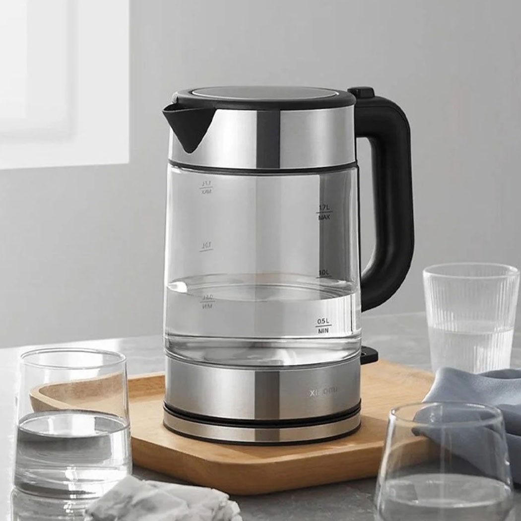 Chaleira elétrica transparente com base e tampa em aço inoxidável e pega preta sobre bandeja de madeira