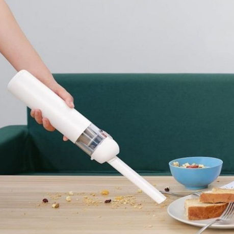 Aspirador portátil de mão branco a limpar migalhas numa mesa de madeira