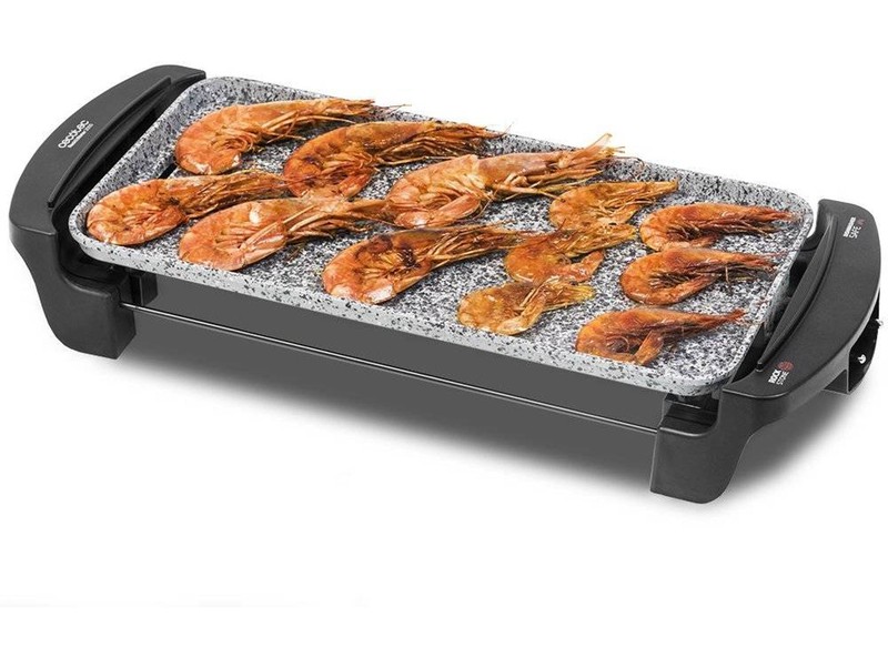 Grill elétrico retangular com camarões grelhados na superfície de pedra cinzenta.