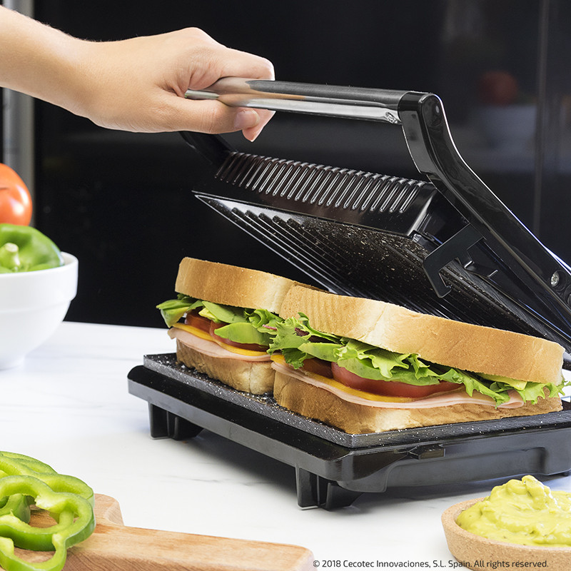 Sanduicheira preta a grelhar um sanduíche com alface, tomate e fiambre numa cozinha