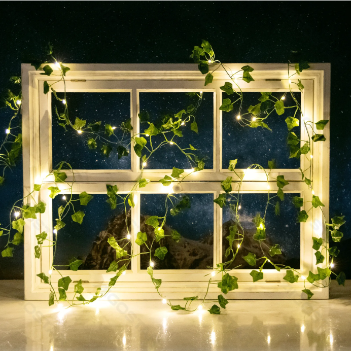 Janela branca decorada com luzes LED e folhagem verde à noite