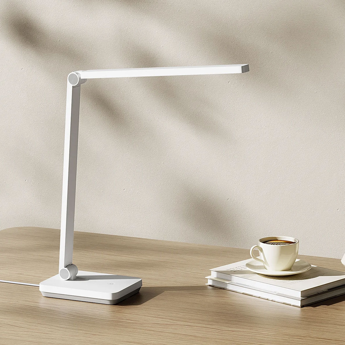 Candeeiro de secretária branco minimalista com chávena de café e livros numa mesa de madeira.