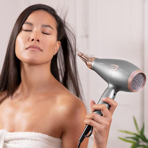 Mulher com secador de cabelo cinzento e rosa dourado com cabelo castanho e toalha branca