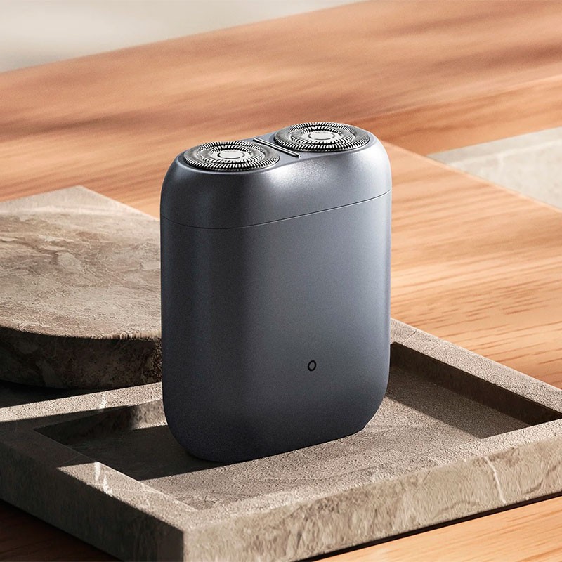 Aparelho de barbear eléctrico cinzento escuro com duas cabeças rotativas em tabuleiro de pedra