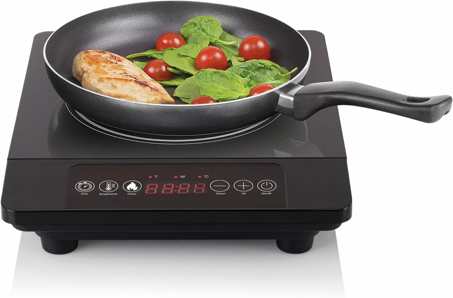 Fogão elétrico preto com frigideira contendo frango, folhas verdes e tomates-cereja