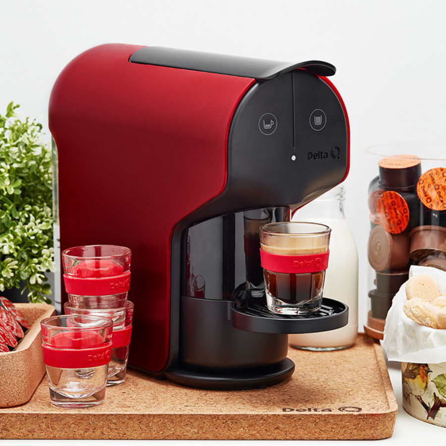 Máquina de café vermelha e preta Delta Q com copos de vidro num tabuleiro de cortiça
