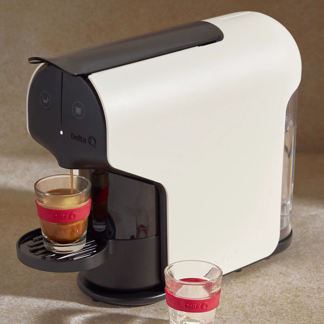 Máquina de café Delta Q a preparar café em chávena de vidro com pega vermelha