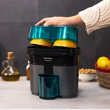 Espremedor de citrinos elétrico com duas metades de laranja em cima, bancada de cozinha cinza