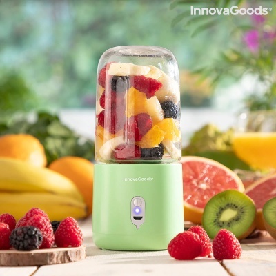 Liquidificador portátil verde com frutas dentro e frutas ao redor em superfície de madeira