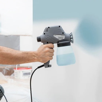 Pistola de pintura elétrica cinzenta com reservatório translúcido, em uso