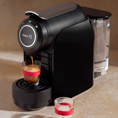 Máquina de café expresso Delta Q preta com copo de vidro a receber café