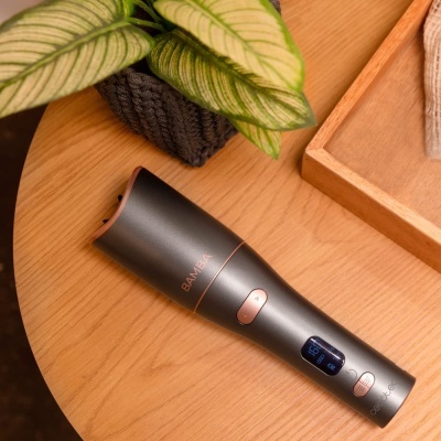 Aparelho de barbear elétrico cinzento BAMBA sobre mesa de madeira ao lado de planta