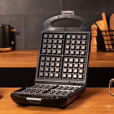 Máquina de waffles preta aberta numa cozinha com bancada de madeira