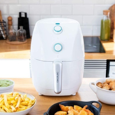 Máquina de cozinha branca Cecotec com botões azuis numa bancada de madeira com pratos de comida