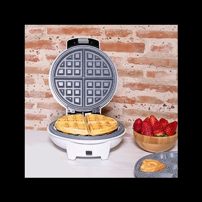 Máquina de waffles branca aberta com waffles dourados e tigela de morangos ao lado numa bancada