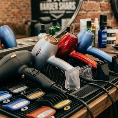 Secadores de cabelo e acessórios de barbearia sobre mesa de madeira com parede de tijolo ao fundo