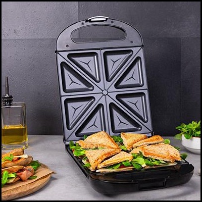 Sanduicheira preta aberta com seis compartimentos triangulares e sanduíches recheados.