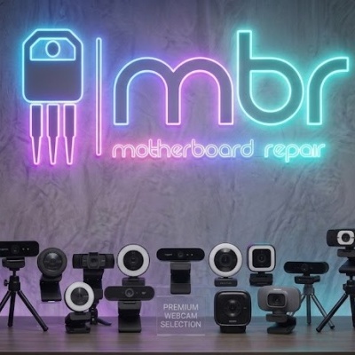 Várias webcams em cima de uma mesa com letreiro de néon mbr motherboard repair ao fundo
