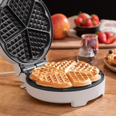 Máquina de waffles aberta com waffles dourados sobre mesa de madeira