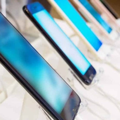 Telemóveis modernos em exposição num balcão branco, ecrãs azuis iluminados.