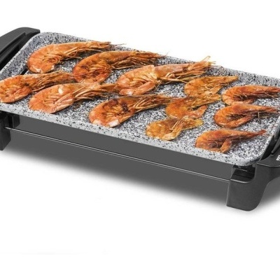 Grill elétrico retangular com camarões grelhados na superfície de pedra cinzenta.