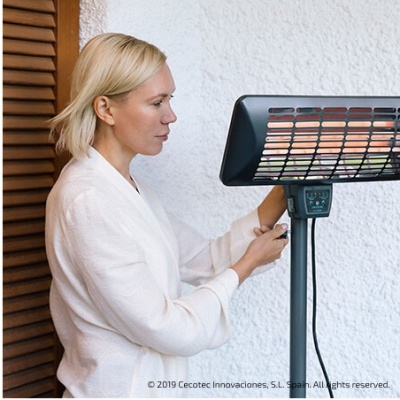 Lareira elétrica preta de pé com painel de controlo, junto a parede branca e porta de madeira, mulher loira a ajustar