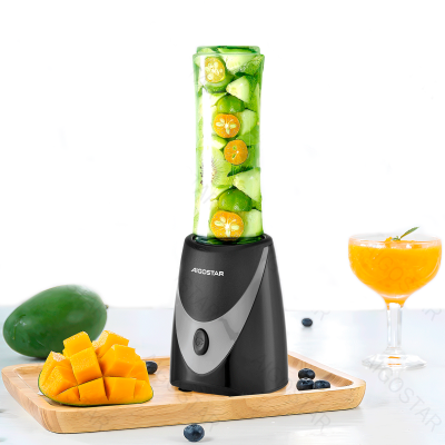 Liquidificador AIGOSTAR preto e cinzento com copo cheio de frutas verdes e laranja numa tábua de madeira com manga e mirtilos, copo de sumo laranja.