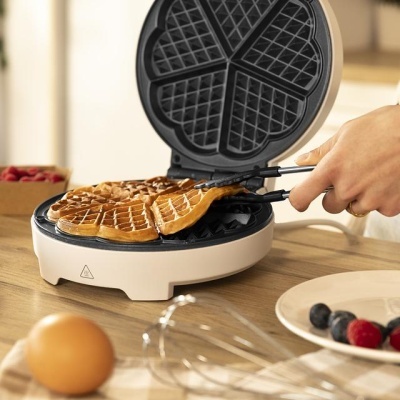 Máquina de waffles branca a cozinhar waffles em formato de coração em bancada de madeira