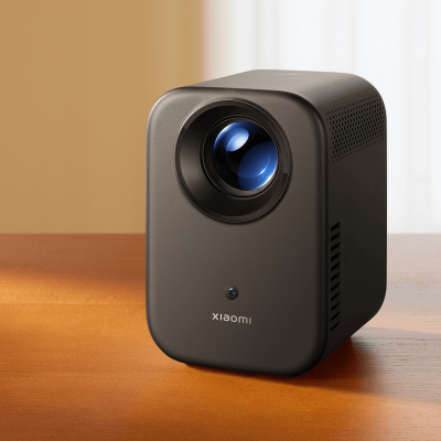 Projetor preto compacto Xiaomi com lente azul numa mesa de madeira