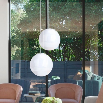 Lâmpadas pendentes brancas redondas numa sala moderna com cadeiras cor-de-rosa e mesa branca, vista para jardim com cerca azul