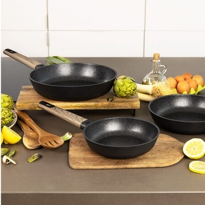 Três frigideiras pretas com cabos de madeira em bancada com ingredientes variados