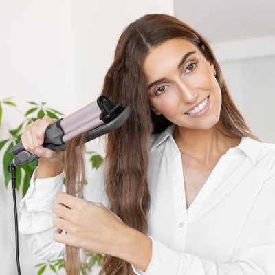 Mulher usa modelador de cabelo elétrico para ondular cabelo castanho