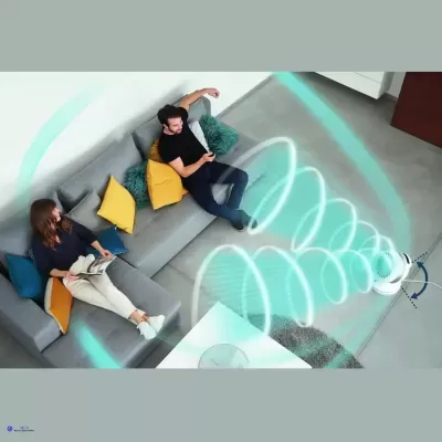 Sofá cinza com almofadas coloridas e duas pessoas sentadas, com dispositivo branco emitindo sinais em espiral.